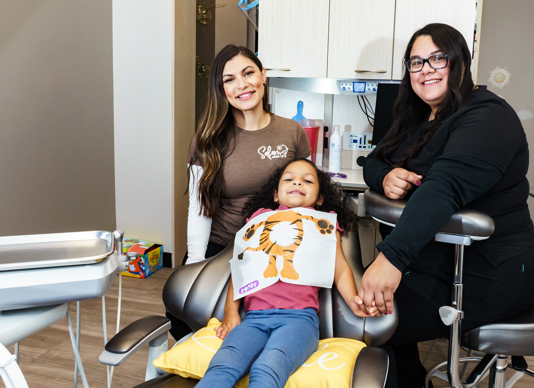 The image features three individuals in a dental office setting, with one person seated on a dental chair and another standing behind her.