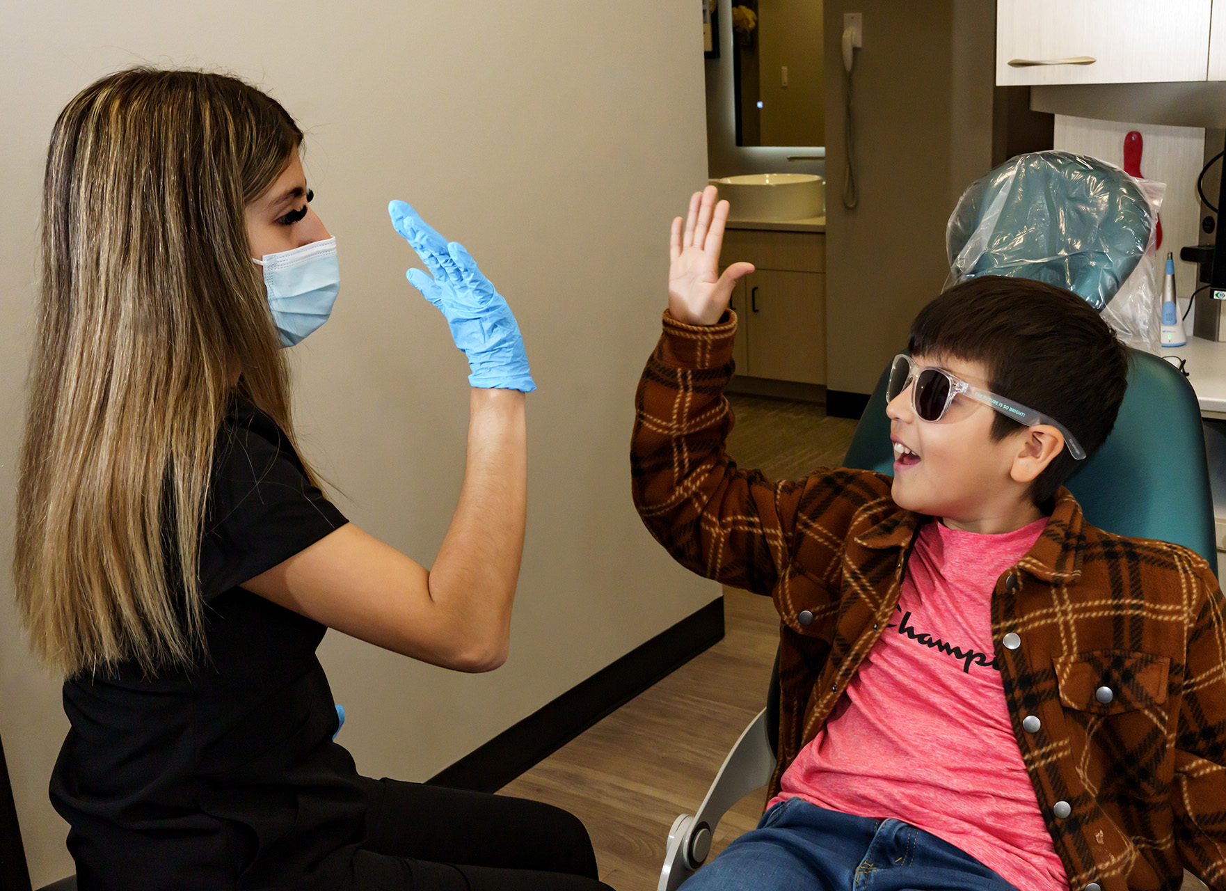 A dental hygienist assisting a young boy in a dental chair, smiling and waving.