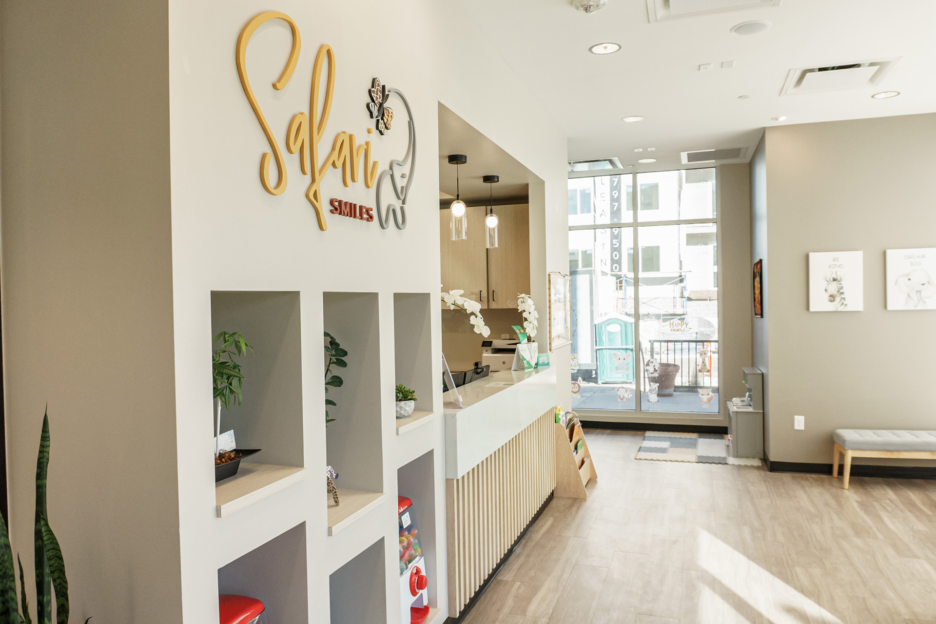 The image shows an interior space, likely a salon or storefront, with a clean and modern design. There is a sign on the wall that reads  SALON  in stylized lettering, and below it, there are shelves displaying various products. The flooring is light-colored, and there s a large window allowing natural light to enter the room. A red fire extinguisher can be seen against one wall, and there s a potted plant on the windowsill.