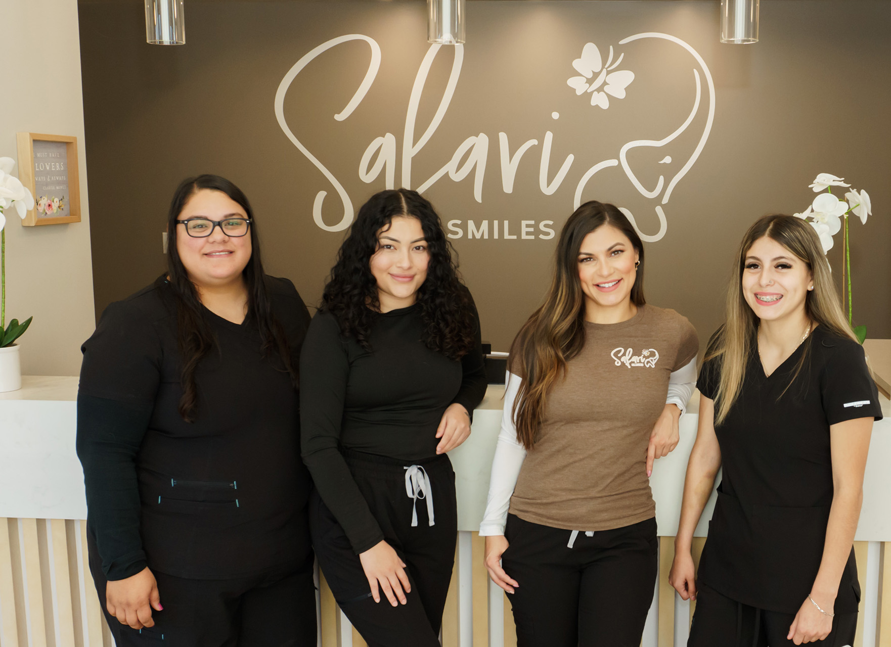 Four individuals standing in front of a sign that reads 'Salavi Smiles' in a dental office setting, posing for the camera.