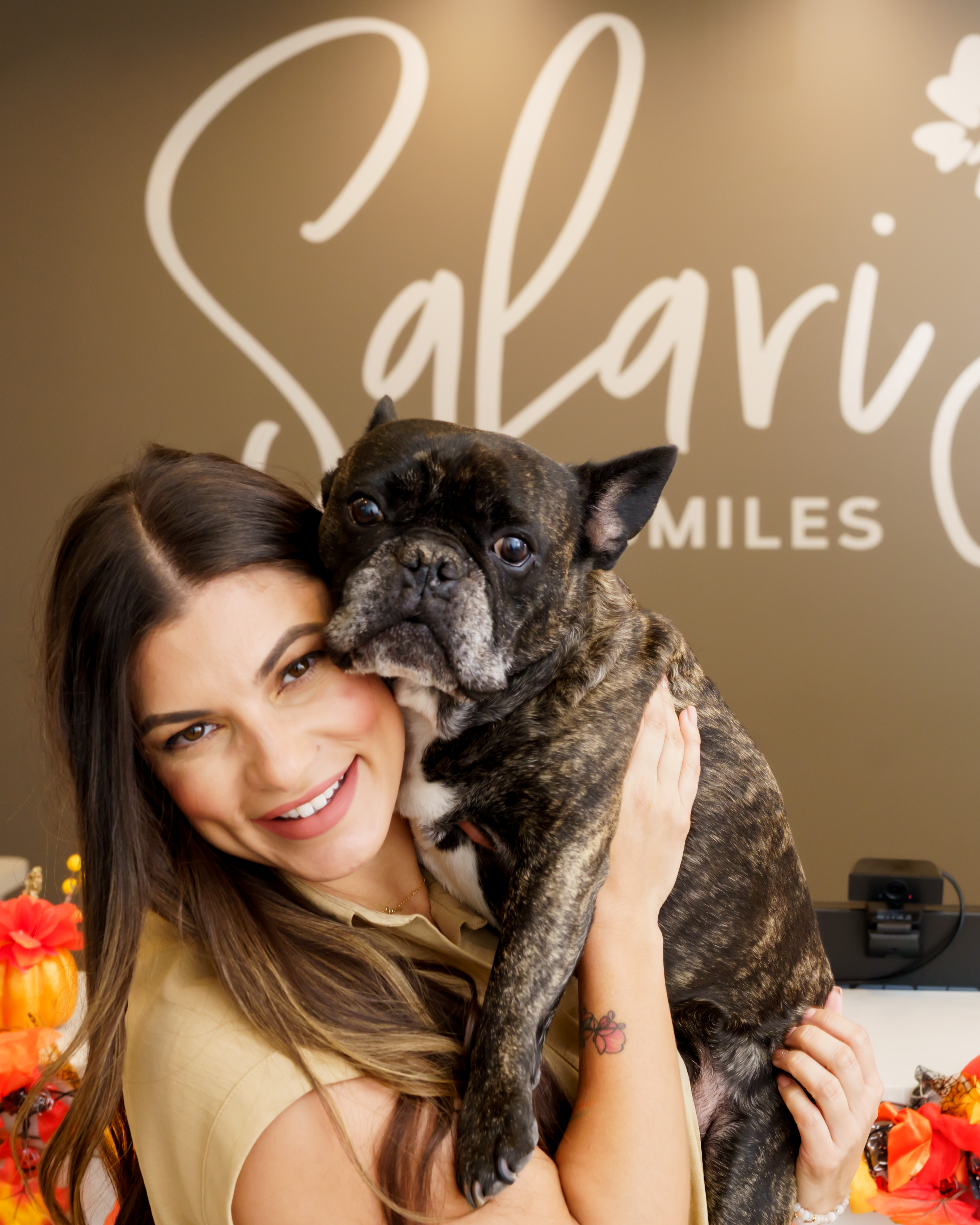 A woman is holding a dog in front of a store sign.