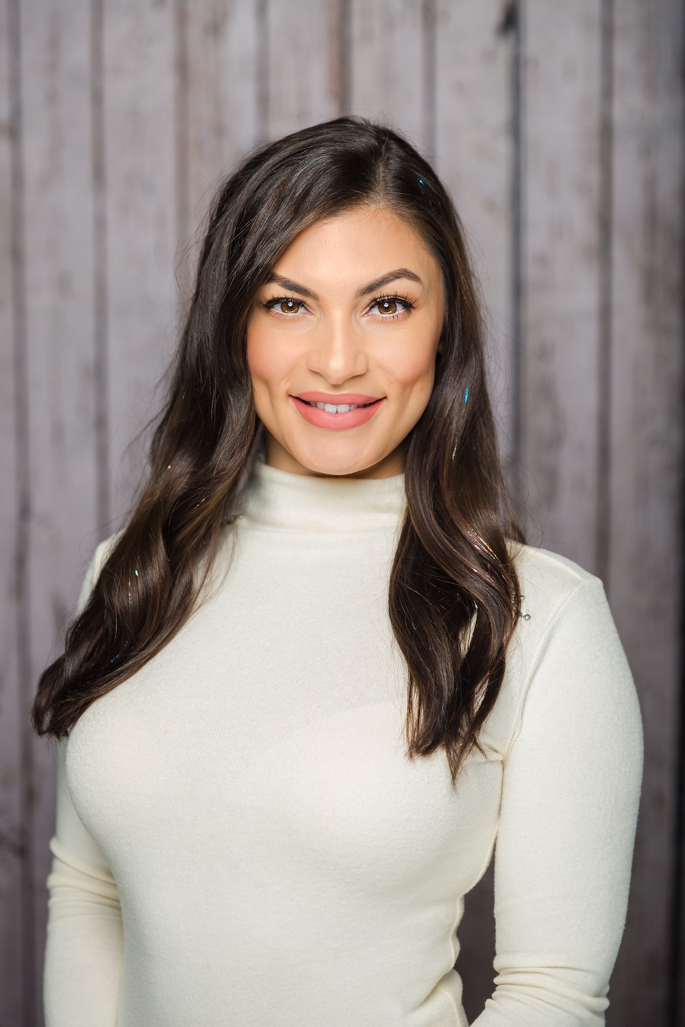 The image shows a woman with a smile, wearing a beige turtleneck sweater and posing for the photo.