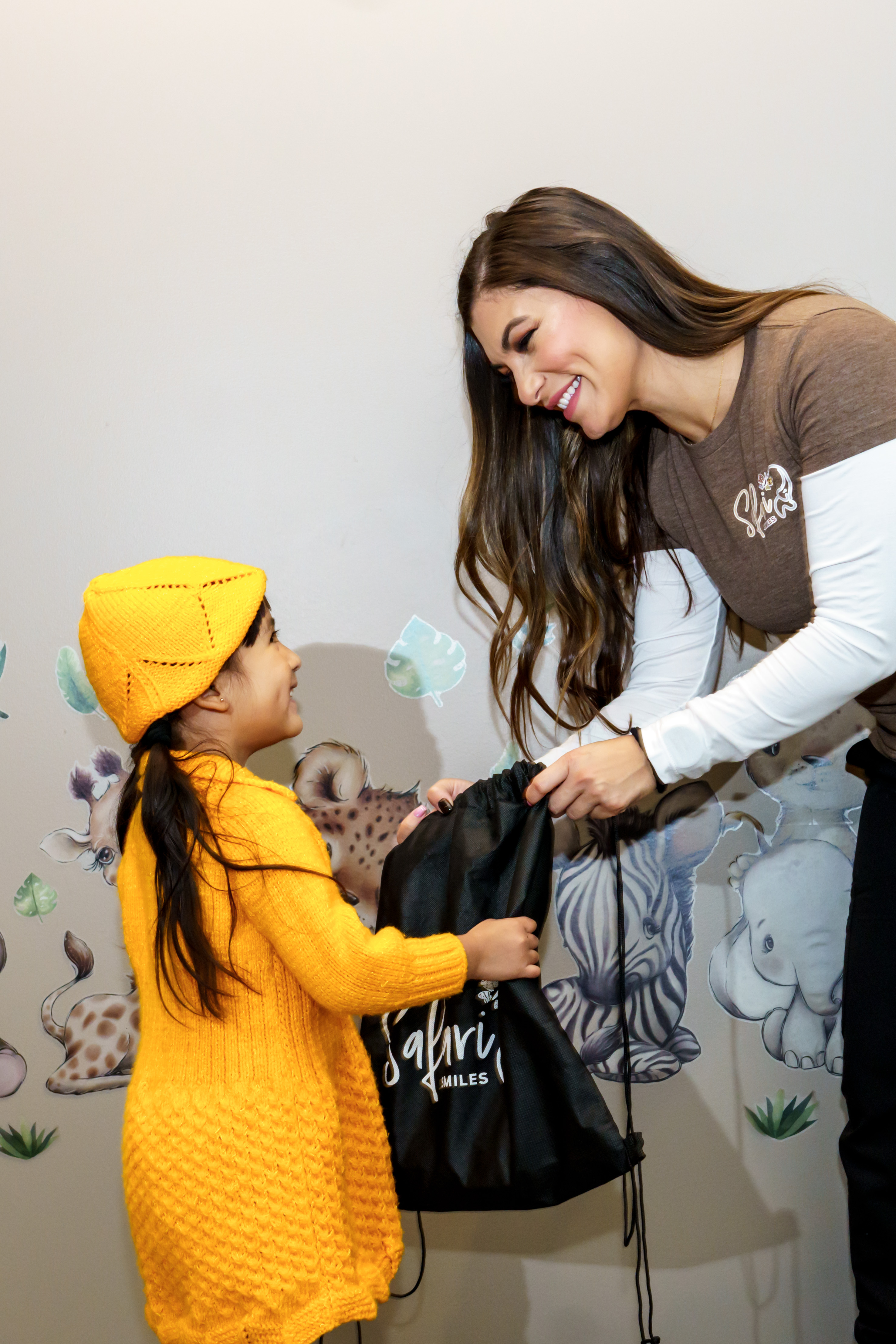 A woman is holding a child's hand and presenting them with a gift bag, likely in a store or at an event.