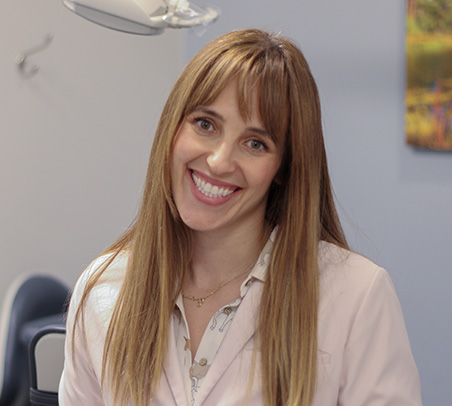 The image shows a woman sitting at a desk, smiling towards the camera.