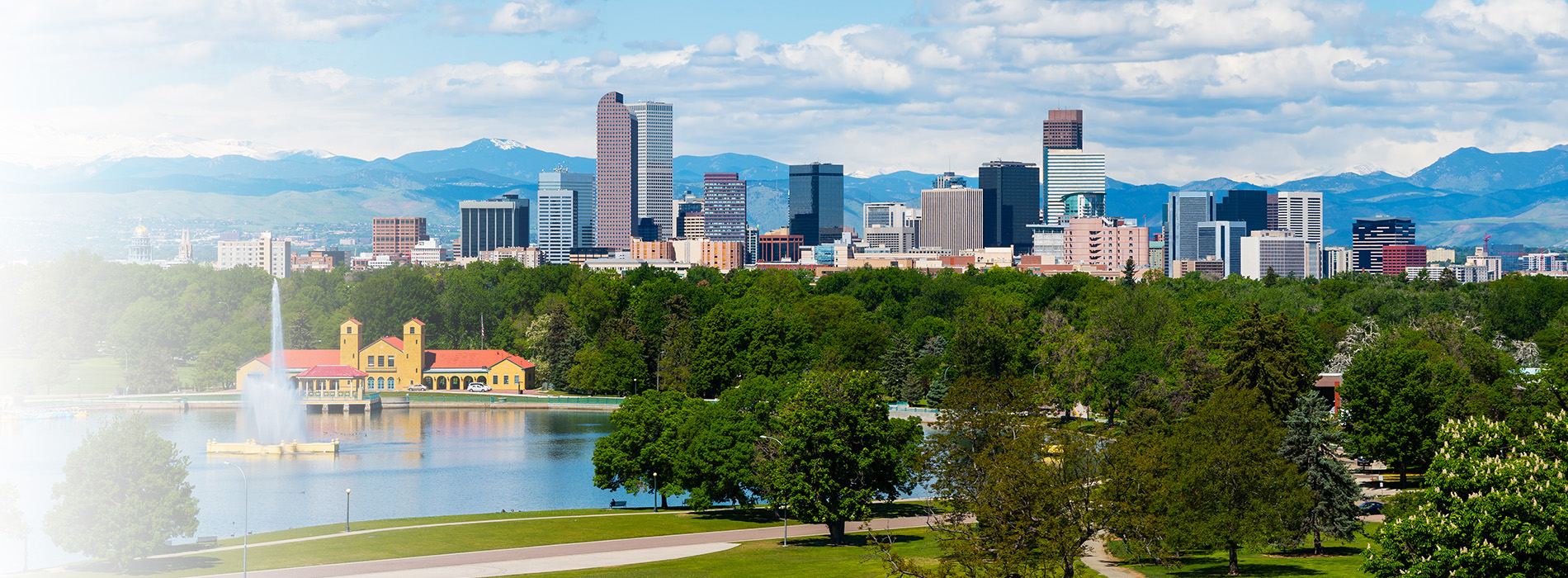 This is a panoramic image of a city skyline with a body of water in the foreground, featuring a large lake and a cityscape with buildings under a partly cloudy sky.