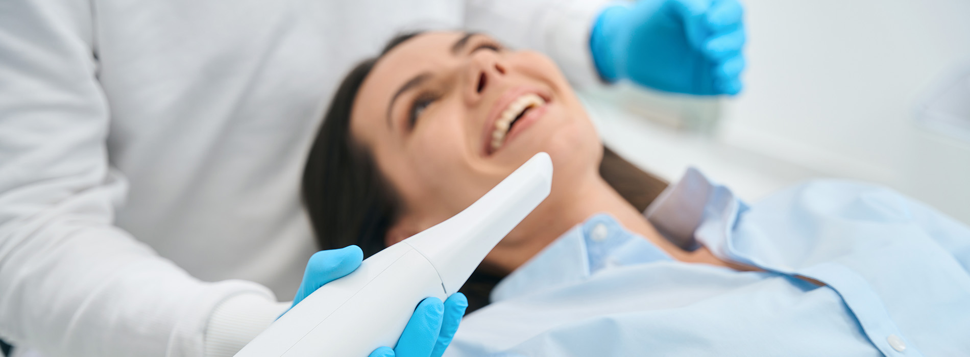 The image shows a person lying on a dental chair, receiving dental care from a professional wearing protective gloves and a mask.