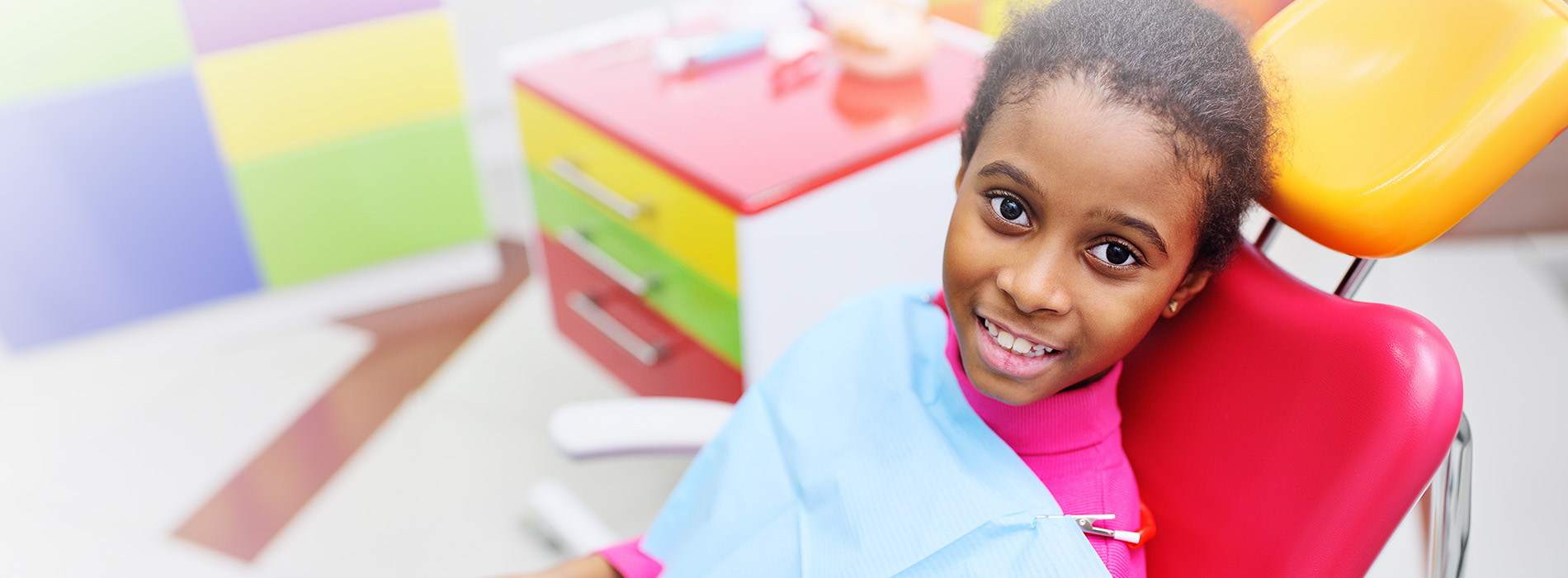 A young girl sitting in a dental chair, smiling at the camera.