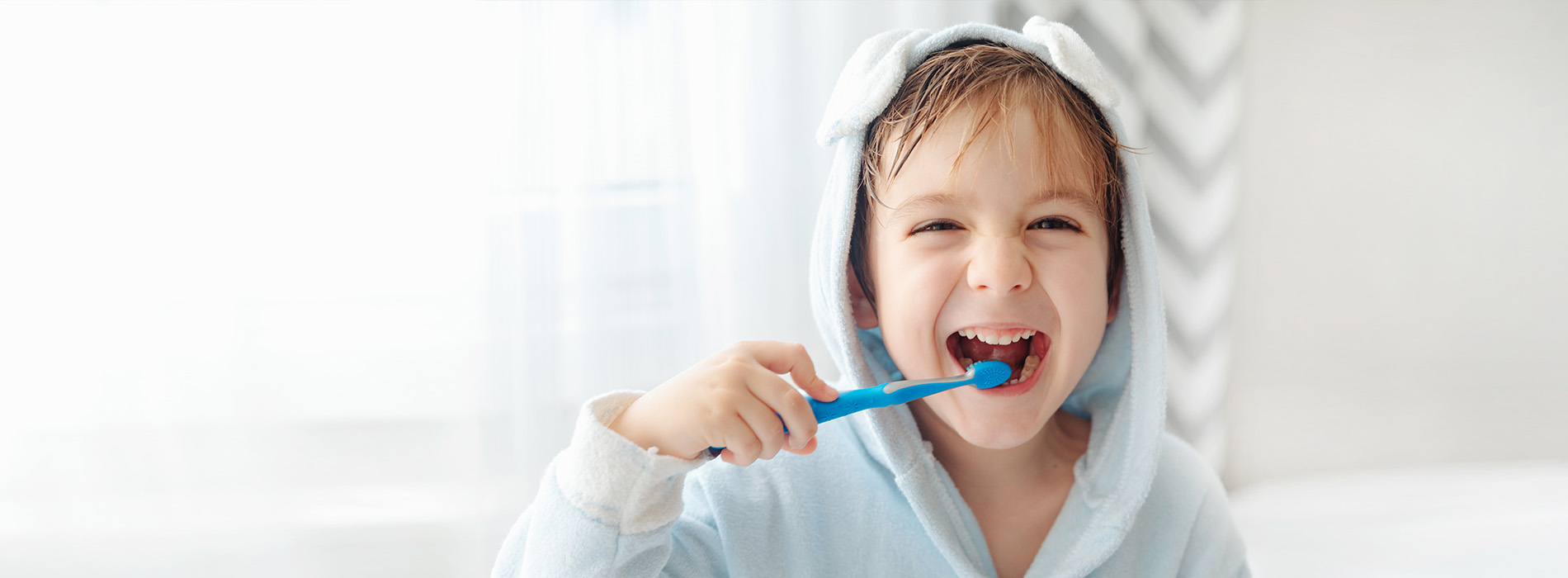 A young child brushing teeth with a blue toothbrush in front of a mirror, captured in a candid moment.