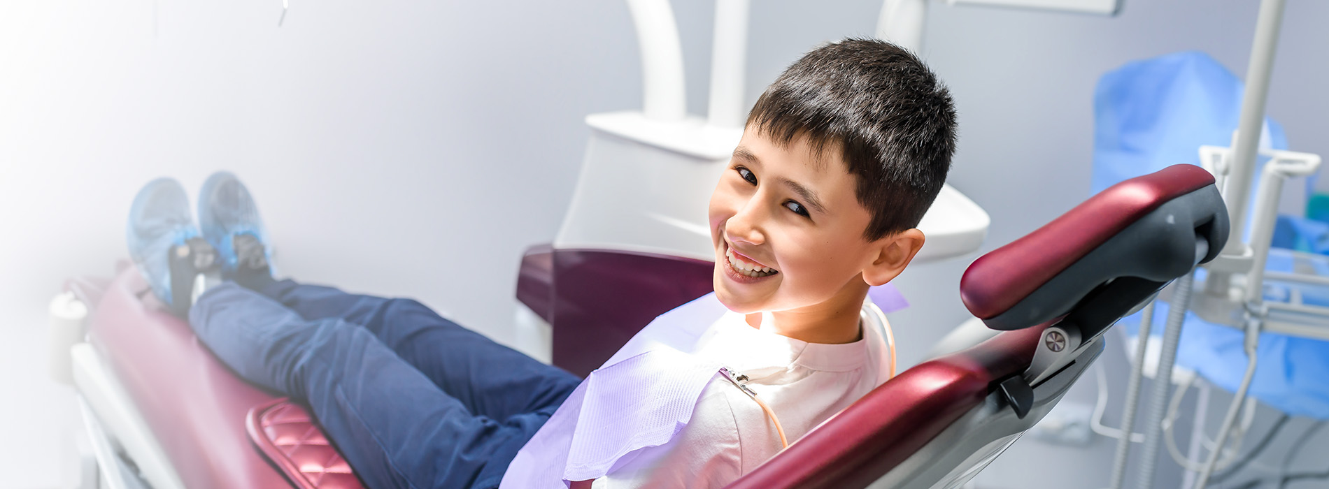 A young boy is sitting in a dental chair, smiling and looking directly at the camera.