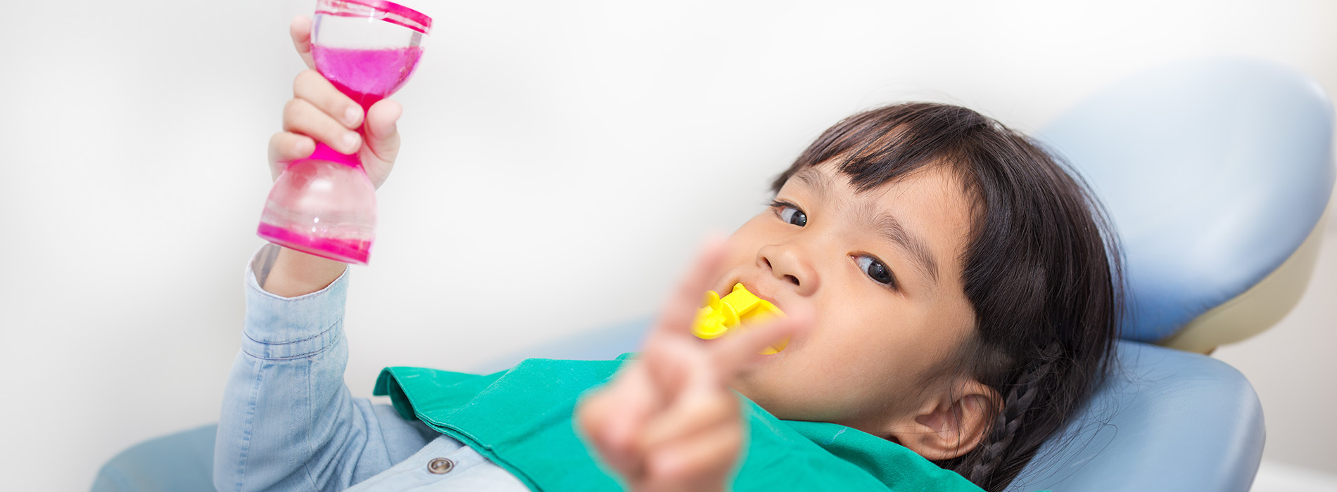 A young child sitting in a dental chair, holding a pink object that could be a toothbrush or a toy.