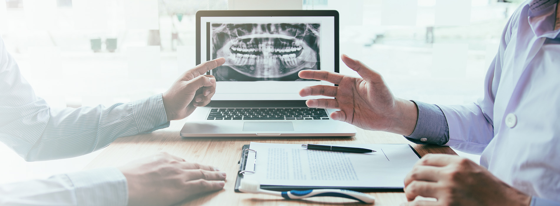 The image shows a professional setting with two individuals, one of whom is gesturing towards a projected medical image while seated at a table with a laptop and papers.