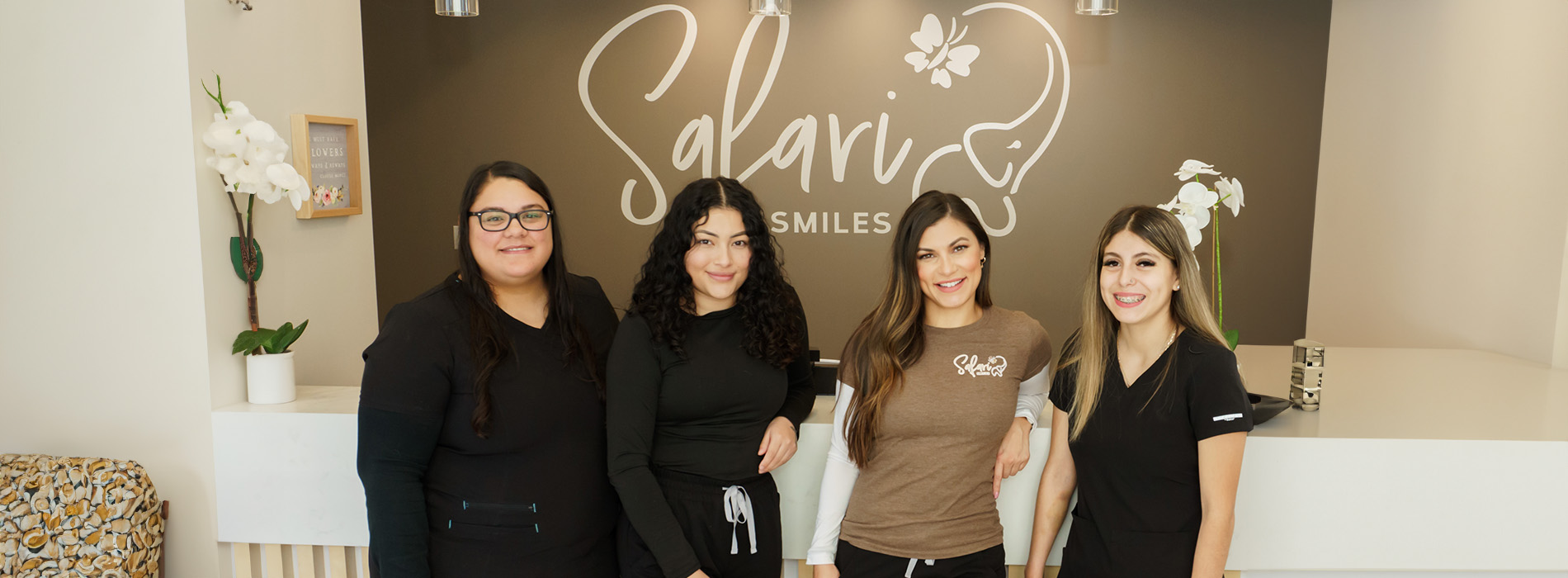 The image shows a group of four individuals posing in front of a storefront with the sign  SALVIO  visible. They are standing in front of a window display, and there is a potted plant on the left side of the frame.