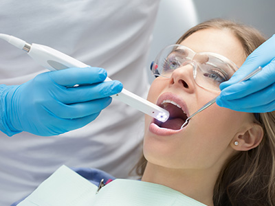 A woman receiving dental treatment, with a dentist using a device to examine her teeth.