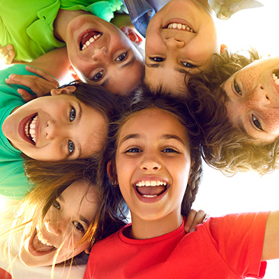 The image shows a group of children, likely at an outdoor event or gathering, smiling and posing for the camera.