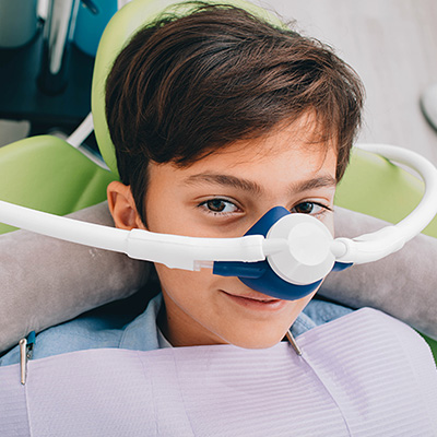 The image shows a young person wearing an oxygen mask and sitting in a dental chair, with the focus on the medical equipment being used.