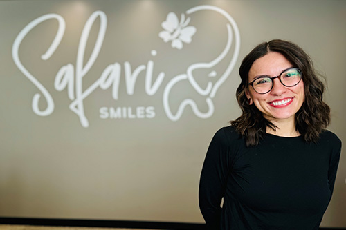 The image features a woman standing in front of a sign that reads  Salavri Smiles.  She is smiling and wearing glasses.