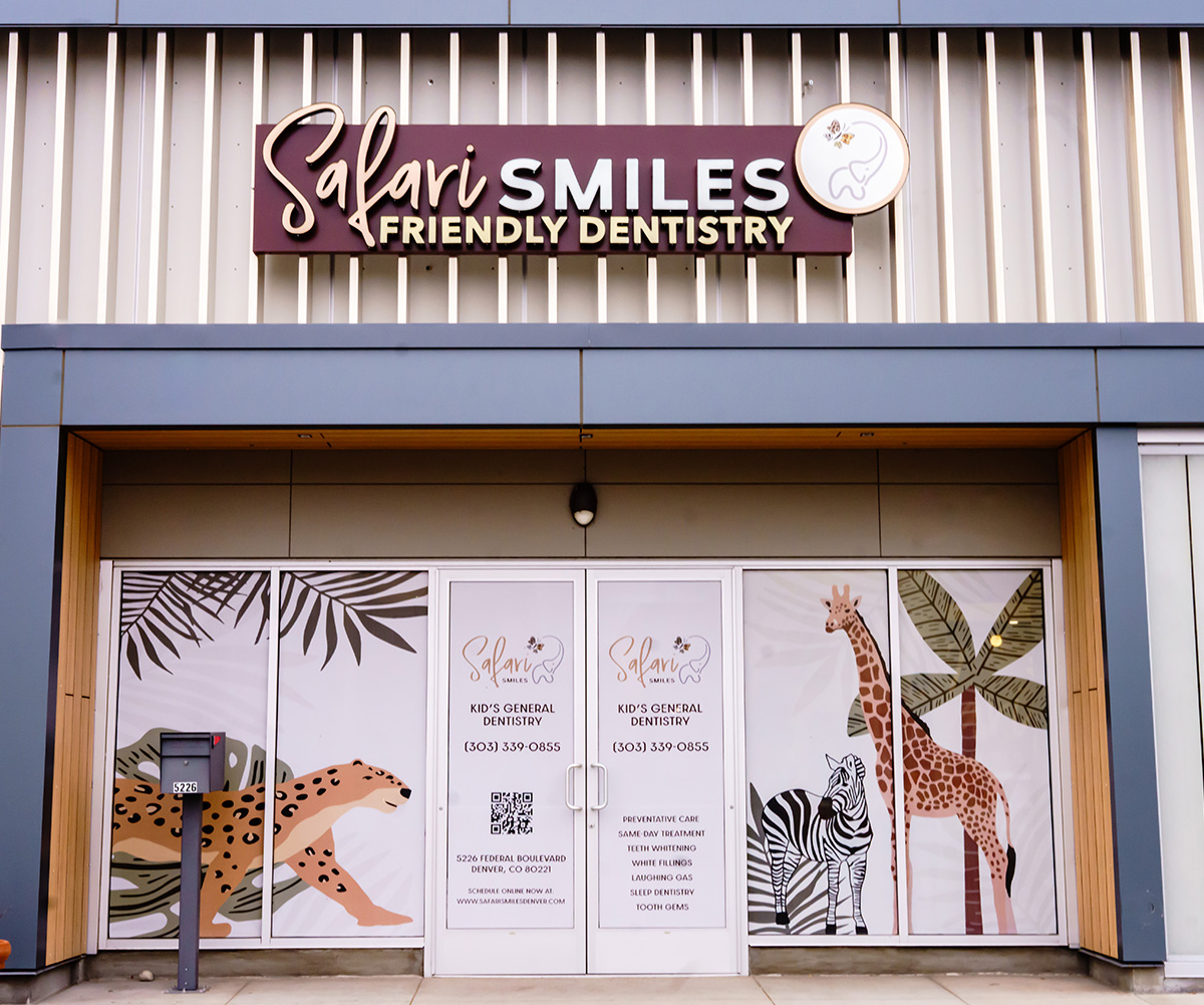 The image shows a sign for  Sali Smiles Friendly Dentistry  with a colorful mural depicting animals and plants behind it.