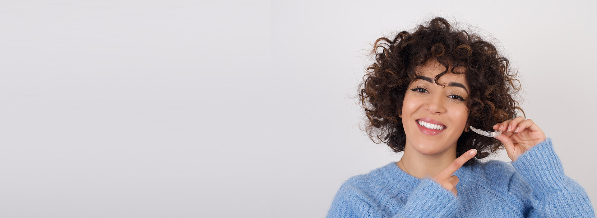 A person with curly hair smiling at the camera, holding a phone to their ear.