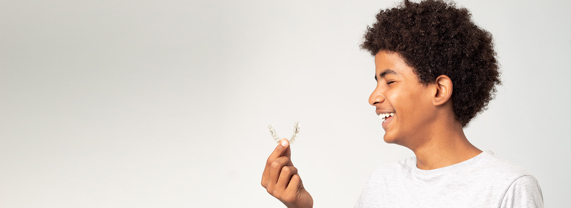 A person is holding a small white flower, smiling and looking upwards.