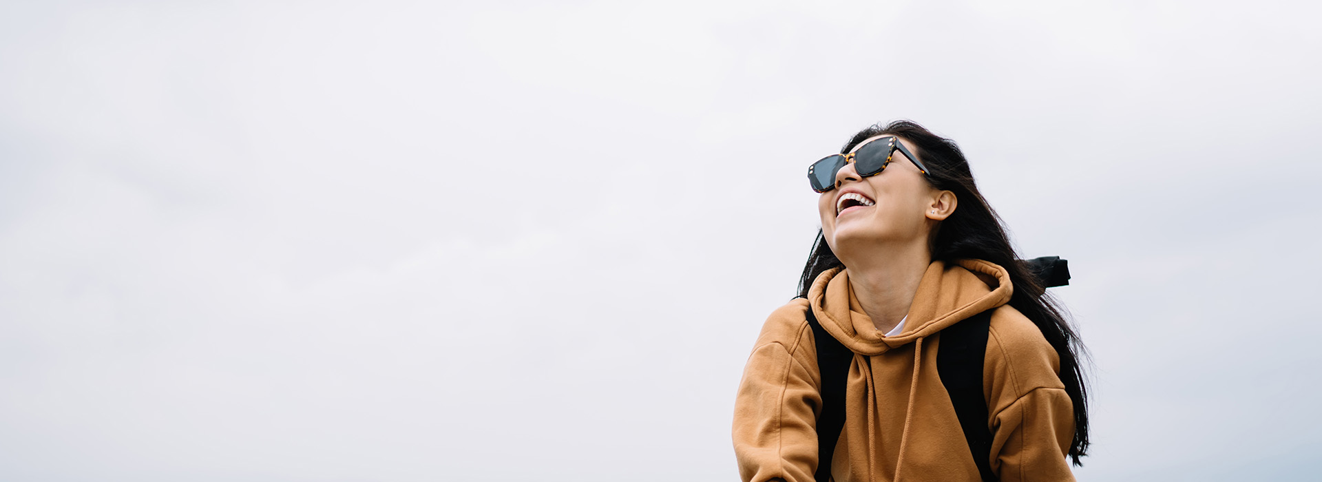 A person in a hoodie stands outdoors, smiling and looking towards the camera.