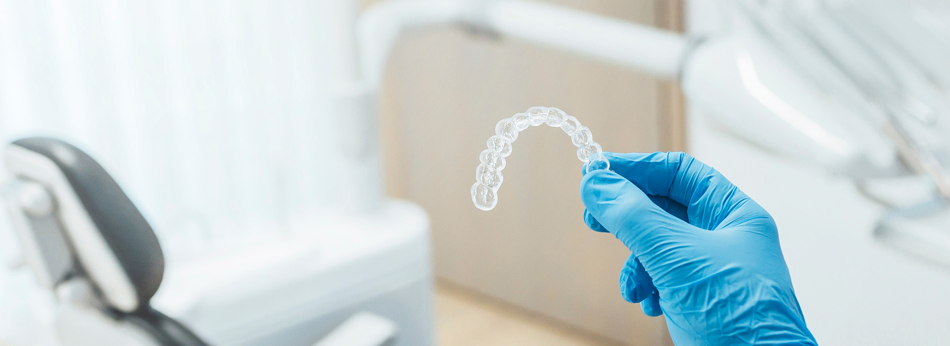 A close-up of a transparent dental impression being held by gloved hands, with a blurred background that suggests a dental office setting.