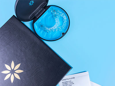 A blue toothbrush in a box with a matching tube of dental floss, placed against a light blue background.