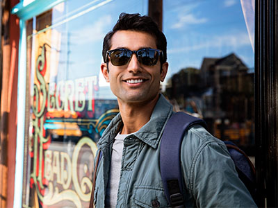 A man with sunglasses and a backpack, standing in front of a storefront window.