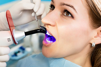 A woman receiving a dental cleaning, with a dental hygienist using an ultrasonic scaler and wearing protective eyewear.