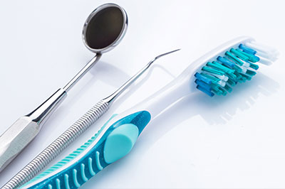 This is an image of dental tools, including a toothbrush with blue bristles and a mouth mirror, placed on a white background.