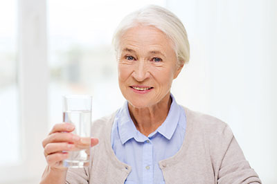 A woman in a blue shirt holding a glass of water, smiling and looking directly at the camera.