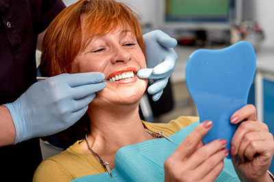 A woman in a dental chair receiving treatment, with a dentist and hygienist attending to her.