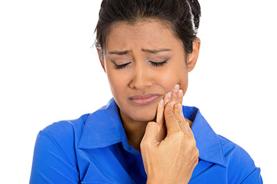 The image shows a person with their eyes closed, holding their face with one hand while the other hand appears to be applying something to their face. They are wearing a blue top and have a concerned or pained expression.