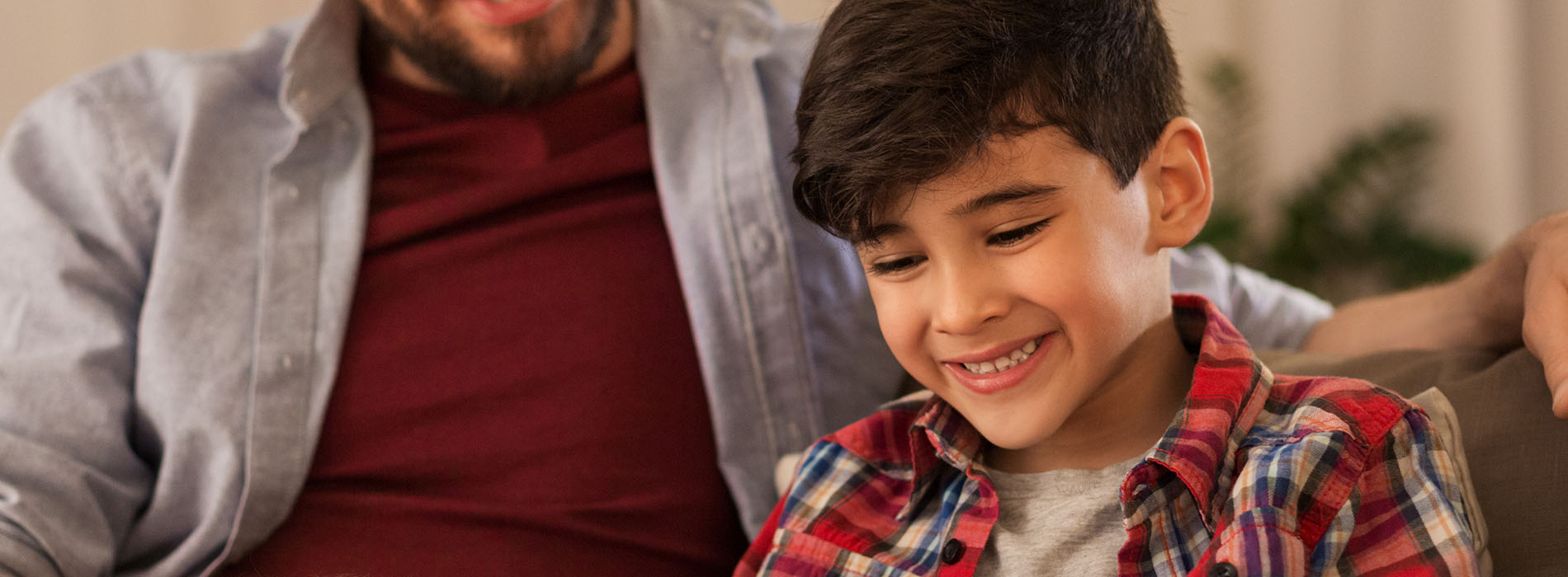 A man and a young boy are seated together, smiling at the camera  they appear to be in a relaxed indoor setting.