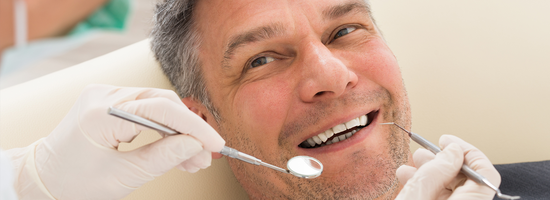 The image shows a man in a dental chair, smiling as he receives dental care.