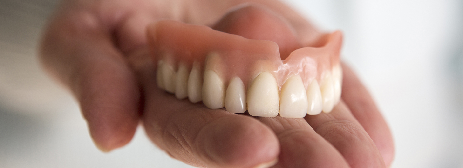 An image of a person holding a set of dentures, with a focus on the dental prostheses.