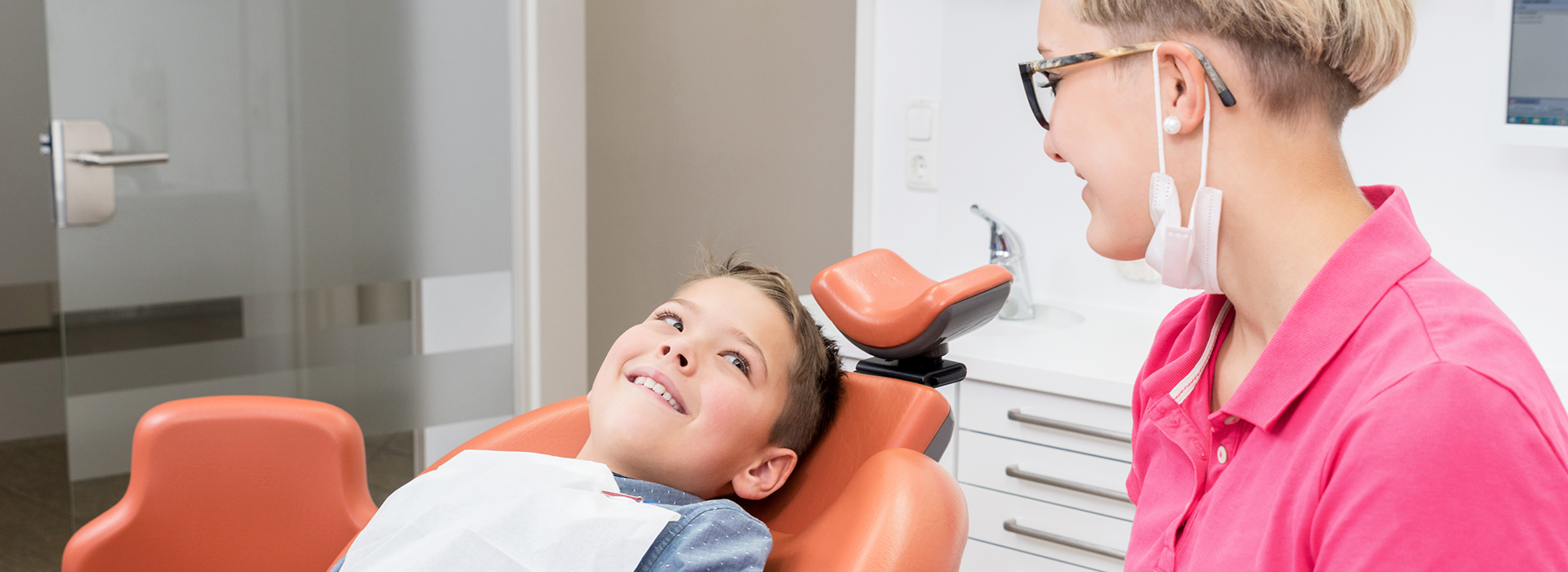 A young child sitting in a dental chair, receiving dental care from an adult.