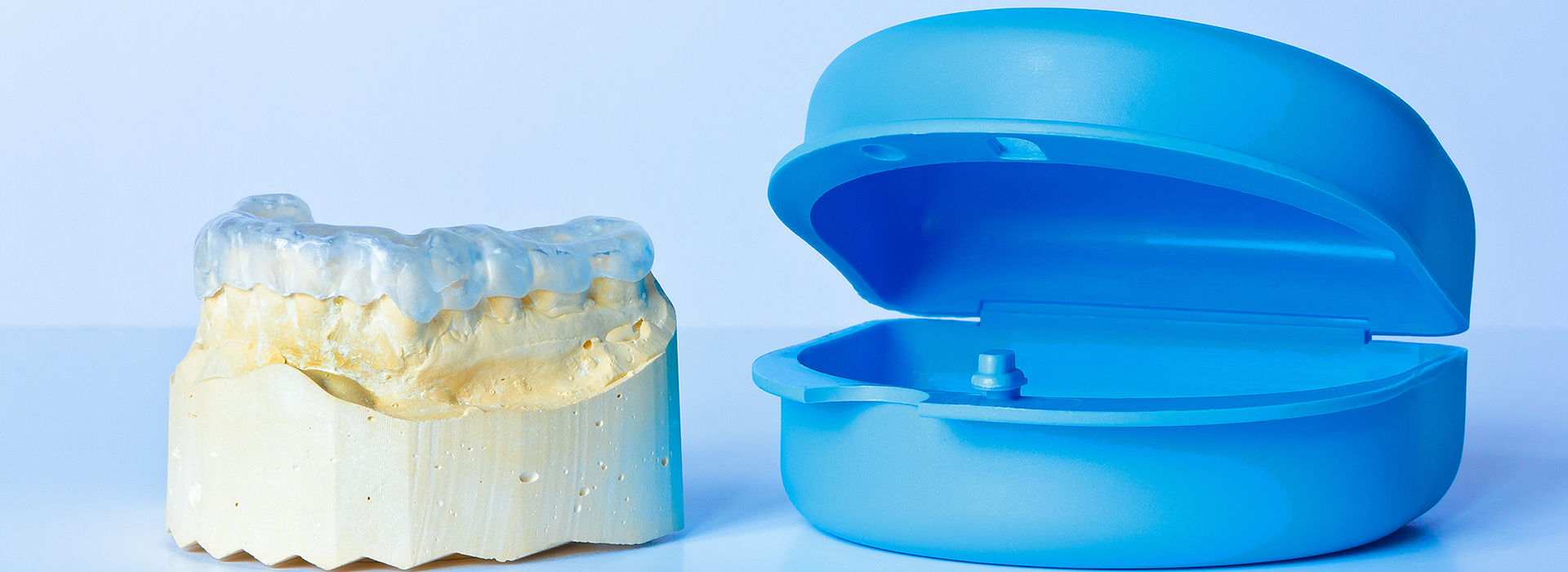 The image shows a blue object, possibly a plastic model or a dental appliance, and a yellow object that appears to be a piece of plastic or a mold, placed side by side against a white background.