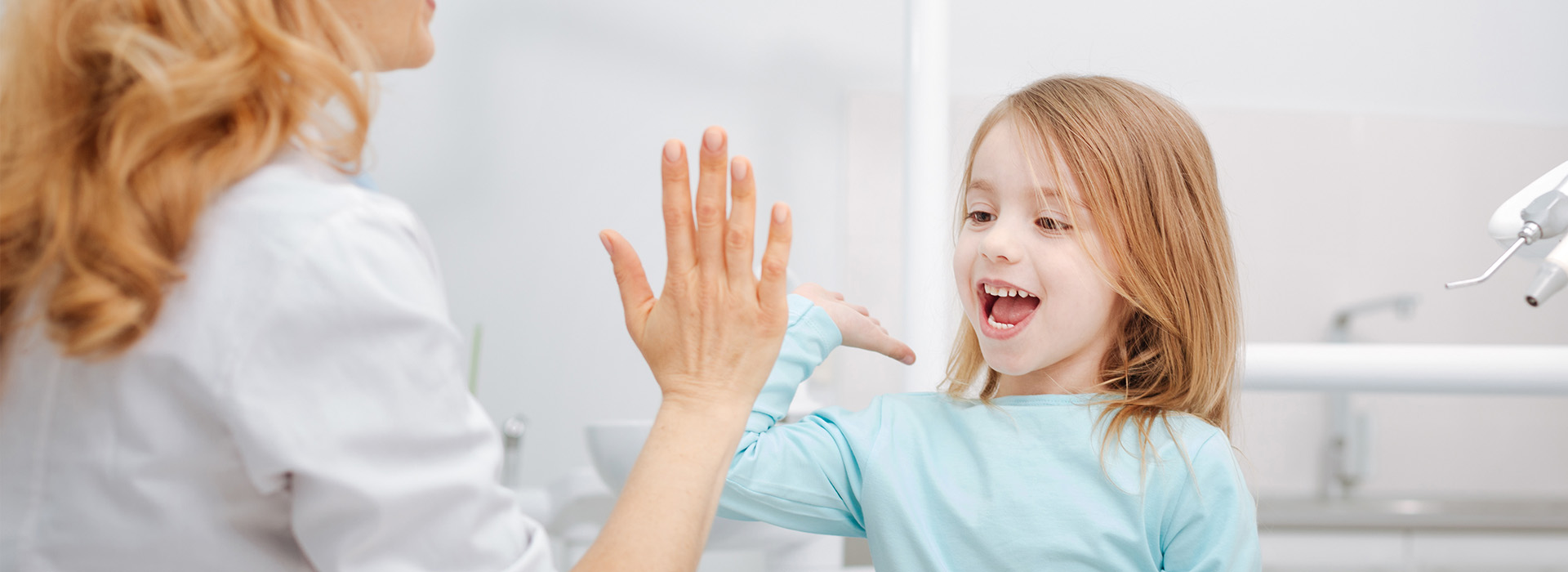 The image shows a woman and a young girl in a dental office setting, with the woman appearing to be interacting with the child.