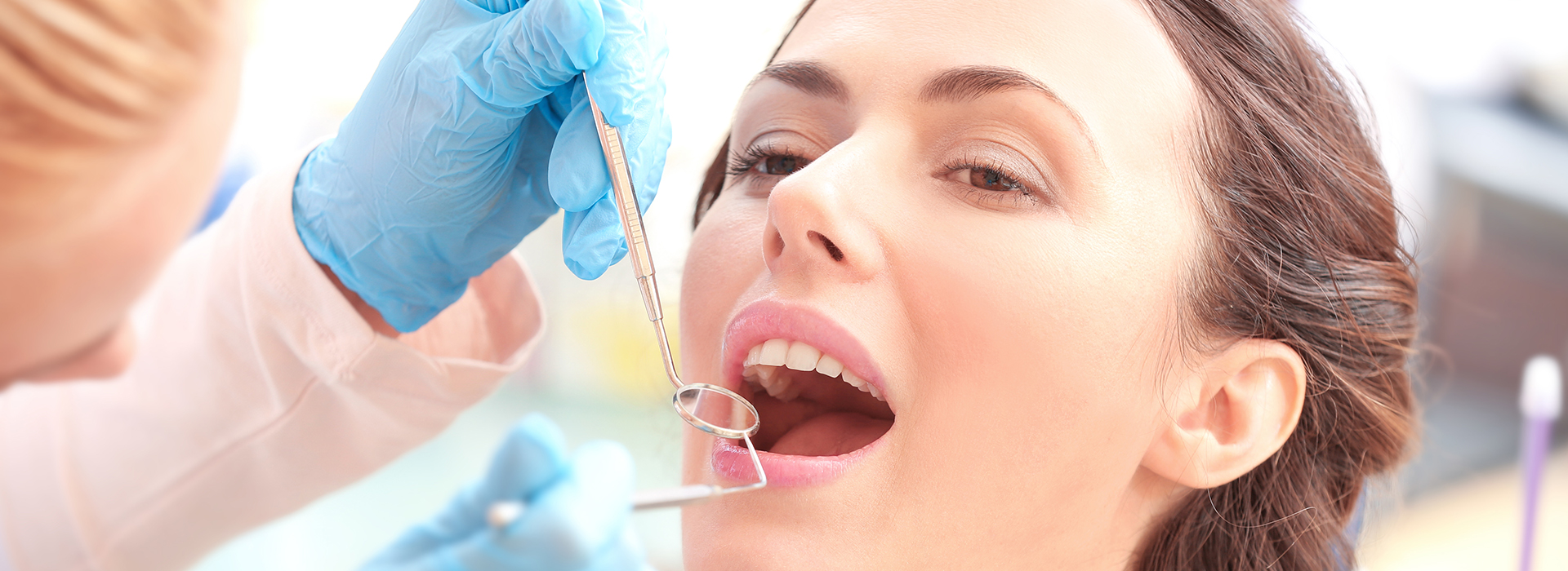 A dental hygienist performing a teeth cleaning procedure on a patient, with the patient s mouth open and the hygienist using specialized tools.