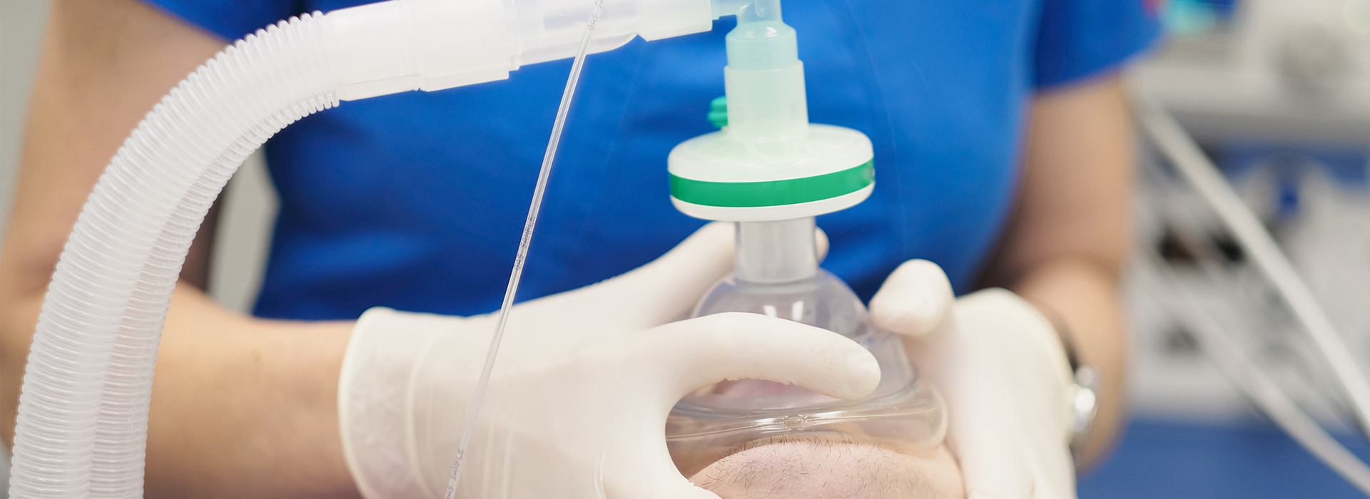 The image shows a person wearing gloves and a blue shirt, focused on a medical device with a clear tube and a green cap, likely in a laboratory or healthcare setting.