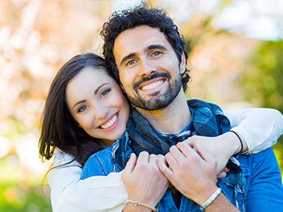 A man and woman embrace in a warm hug, smiling at the camera.