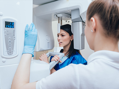 Woman in blue gown and gloves standing next to a woman in a white coat, both examining a large piece of medical equipment.