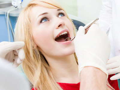 A woman is seated in a dental chair, receiving dental treatment, with a dentist performing the procedure.