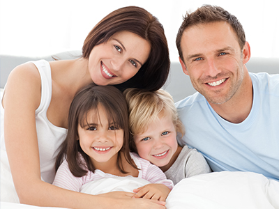 A family of four, including a man, woman, and two children, posing together in bed.