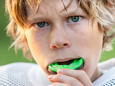 A young male athlete with blonde hair, wearing a football uniform and holding a green sports mouthguard.